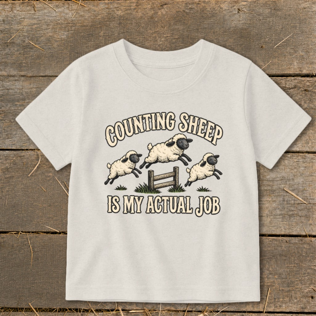 T-shirt with graphic of three sheep jumping over a fence, text reads "Counting Sheep Is My Actual Job."