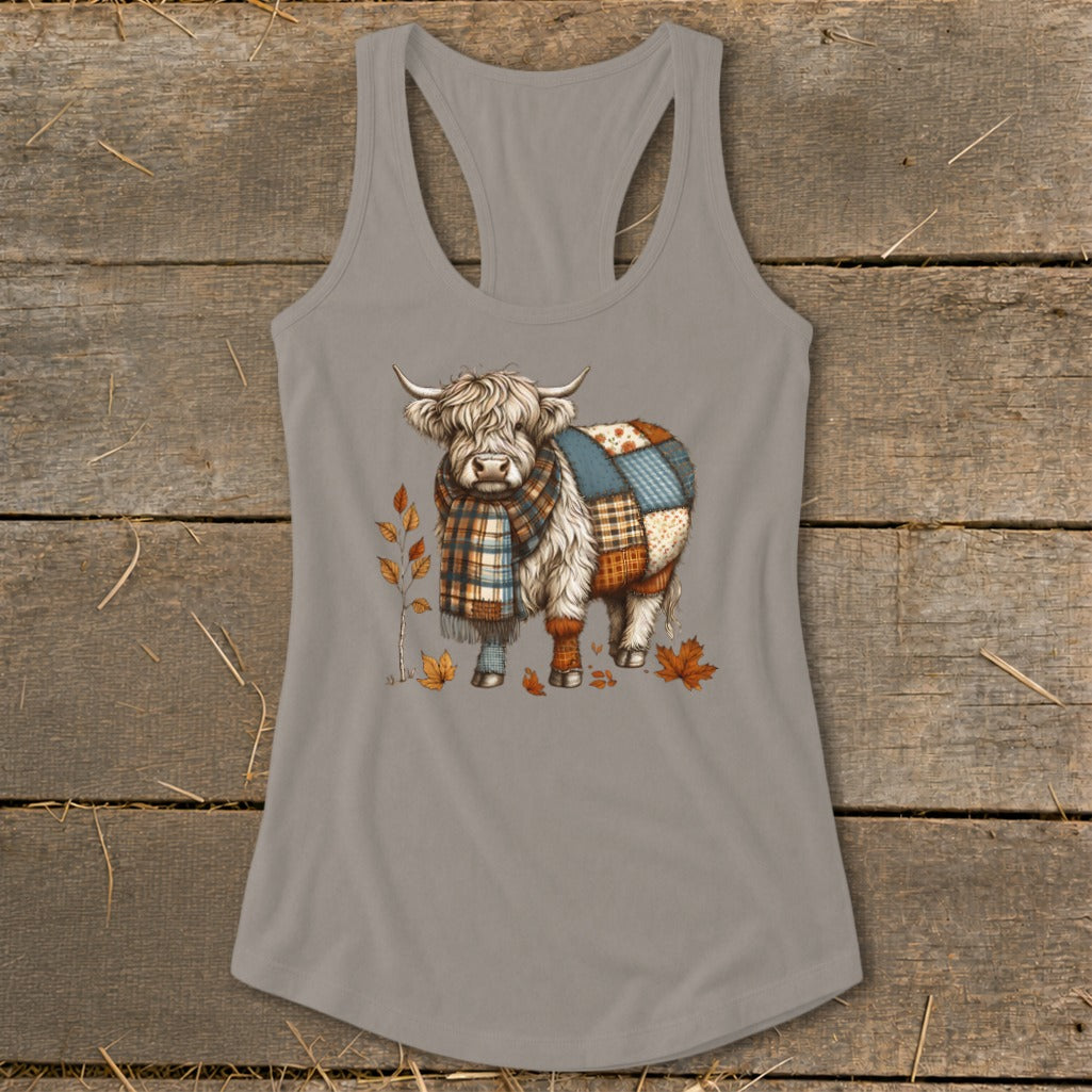 Fluffy Highland cow wearing a plaid scarf and patchwork blanket, with fall leaves.