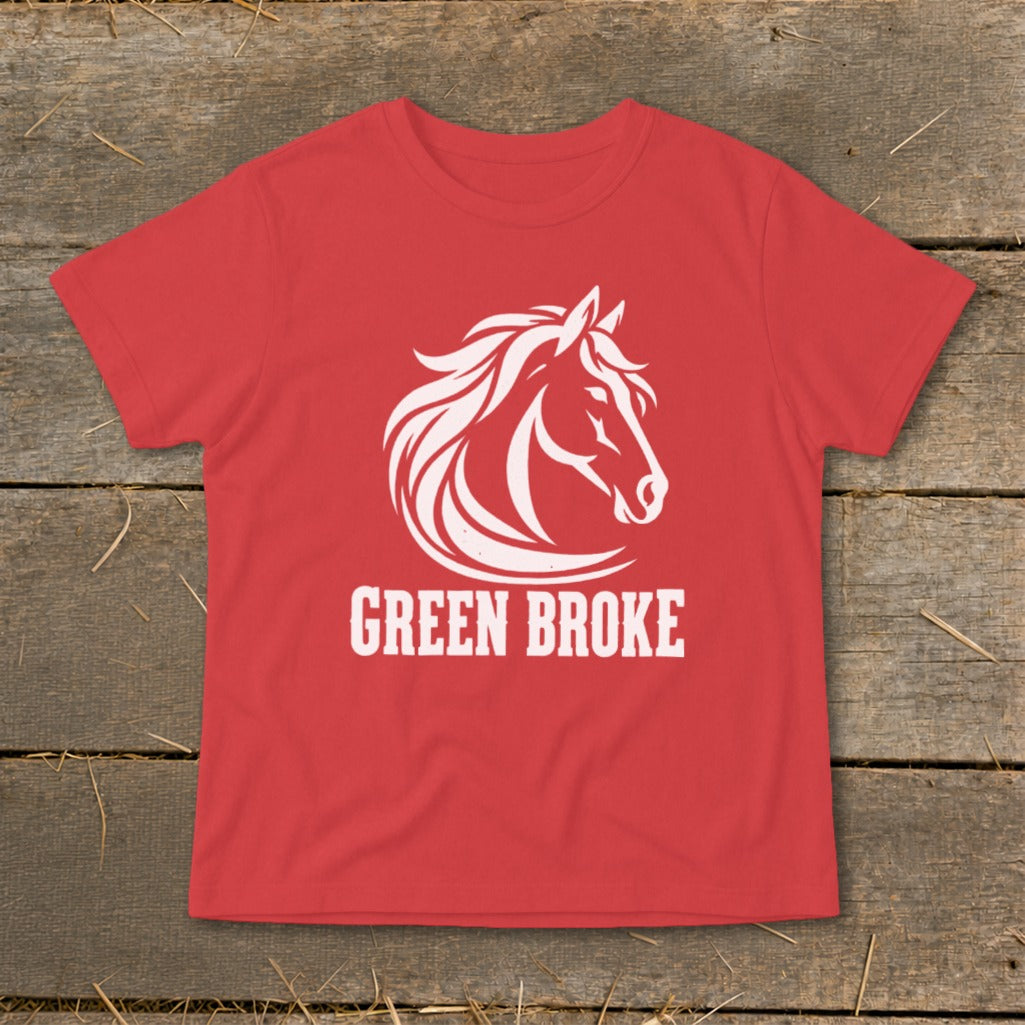 A red t-shirt on a wooden background with a white graphic of a horse and the text GREEN BROKE.