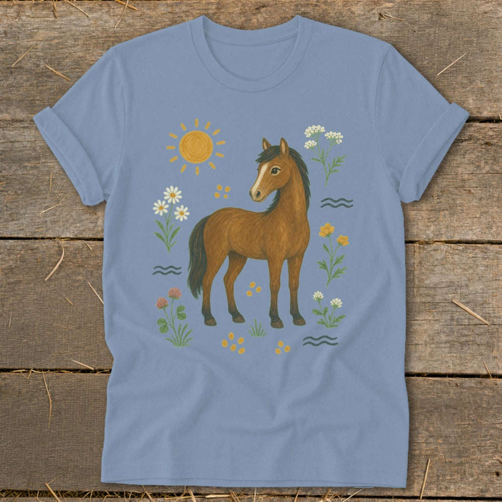 Brown horse surrounded by wildflowers, sun, and wavy lines on a light blue t-shirt.