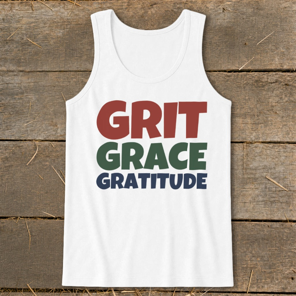A white tank top with the words "GRIT GRACE GRATITUDE" printed in red, green, and blue on a rustic wooden background.