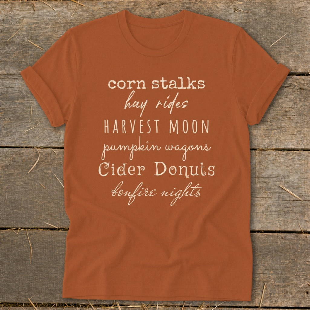 Orange t-shirt with fall-themed text: corn stalks, hay rides, Harvest Moon, pumpkin wagons, Cider Donuts, bonfire nights.