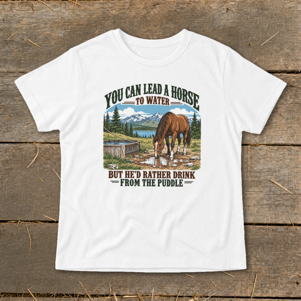 A white t-shirt featuring a graphic of a horse drinking from a puddle with mountains and the text You Can Lead A Horse To Water But He'd Rather Drink From The Puddle.