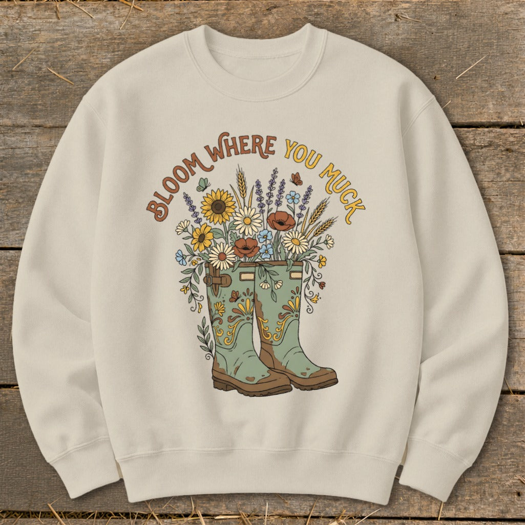 Cream sweatshirt with "Bloom Where You Muck" graphic of flowers in boots.