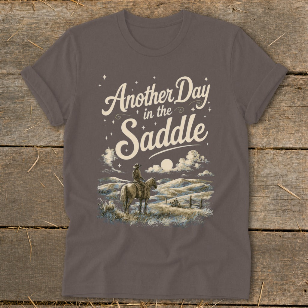 Brown t-shirt with "Another Day in the Saddle" text and cowboy on horseback illustration.