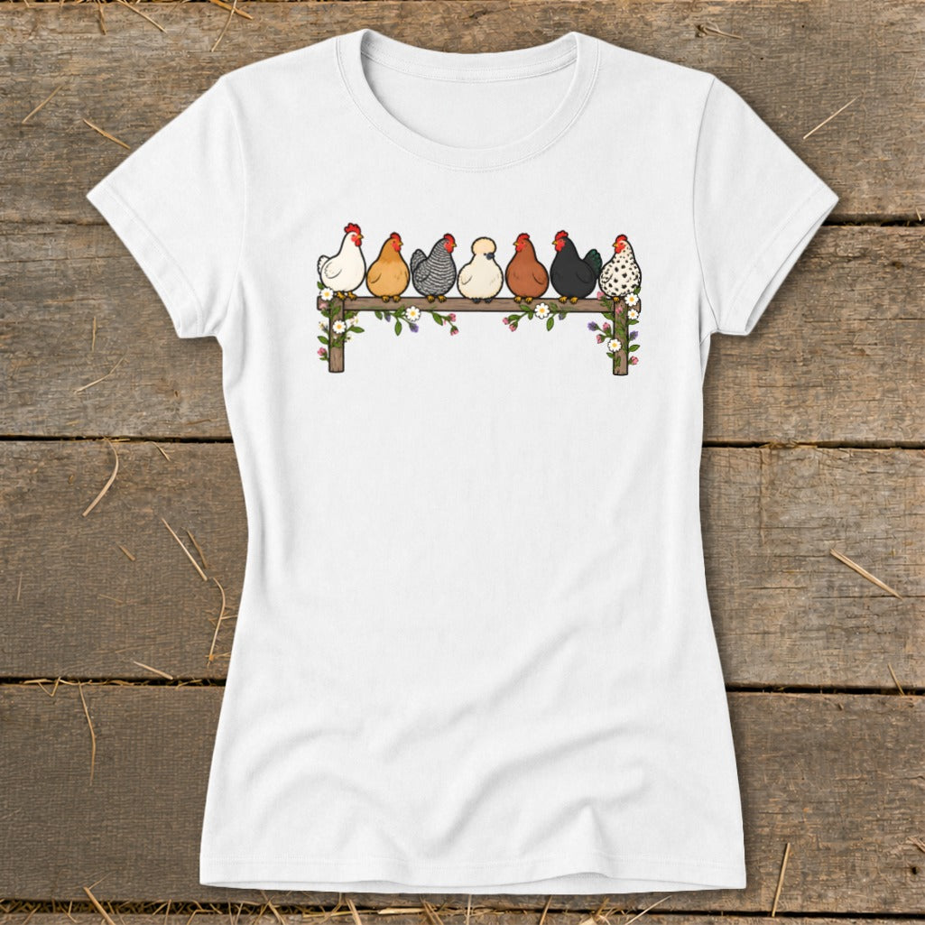A white short-sleeved t-shirt featuring an illustration of seven colorful chickens perched on a flower-decorated wooden fence.
