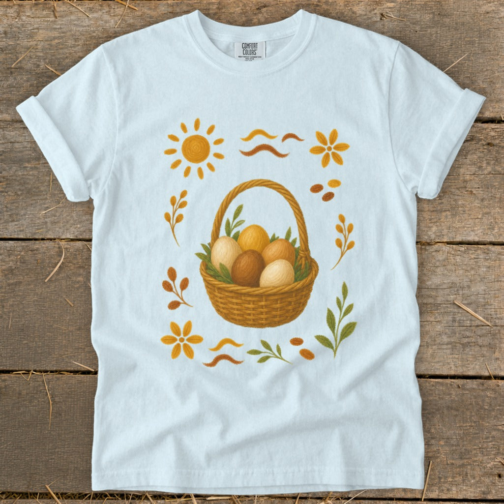 White t-shirt with a woven basket of brown and beige Easter eggs and floral graphics.