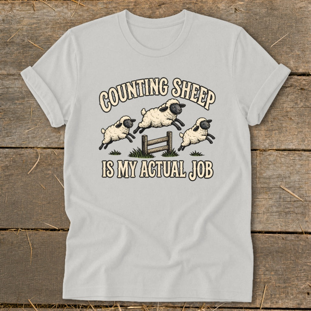 Light grey t-shirt with cartoon sheep jumping over a fence with text "COUNTING SHEEP IS MY ACTUAL JOB".