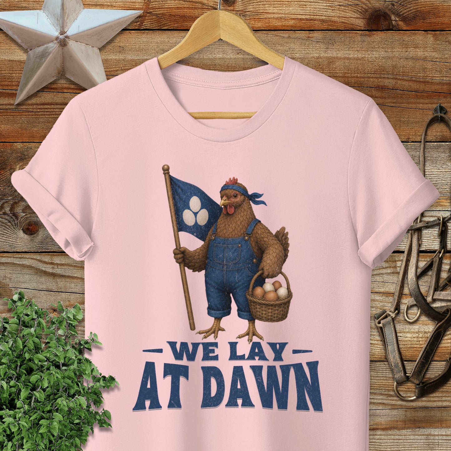 Pink t-shirt with a cartoon chicken holding a flag and basket, text "We Lay At Dawn."