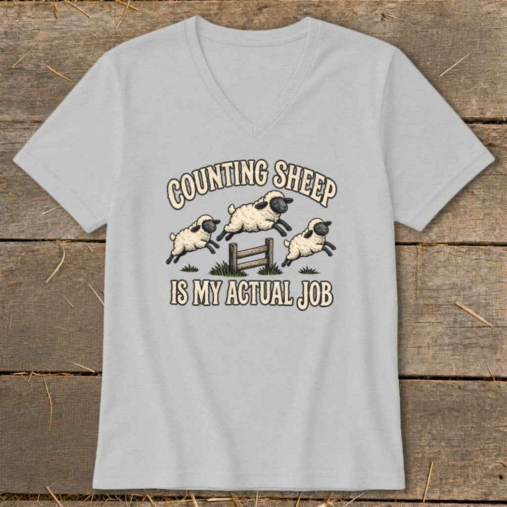 Grey v-neck t-shirt with cartoon sheep jumping over a fence with "Counting Sheep Is My Actual Job" text.
