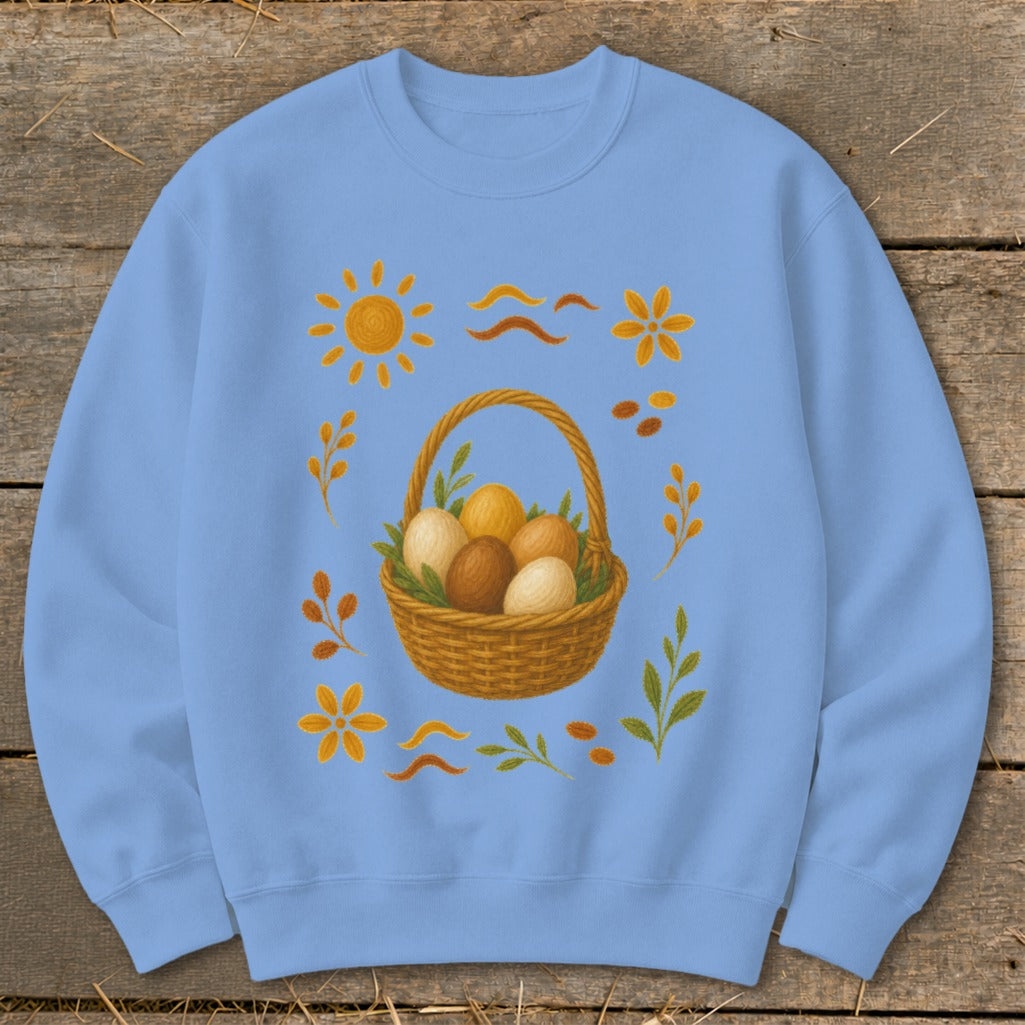 Light blue sweatshirt with a woven basket filled with eggs and surrounding floral and sun graphics.