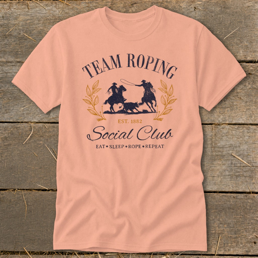 Peach t-shirt with "Team Roping Social Club" graphic and rodeo scene.