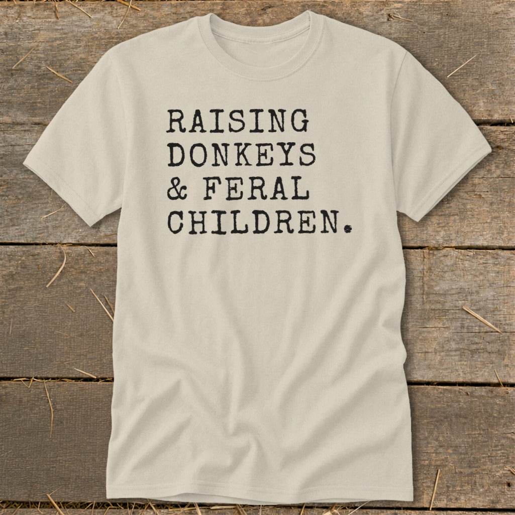Light beige t-shirt with black text: "RAISING DONKEYS & FERAL CHILDREN."