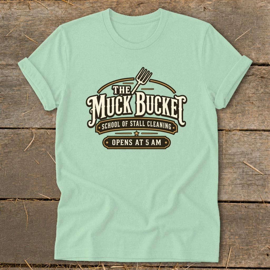 Light blue t-shirt with "The Muck Bucket School of Stall Cleaning Opens at 5 AM" logo.