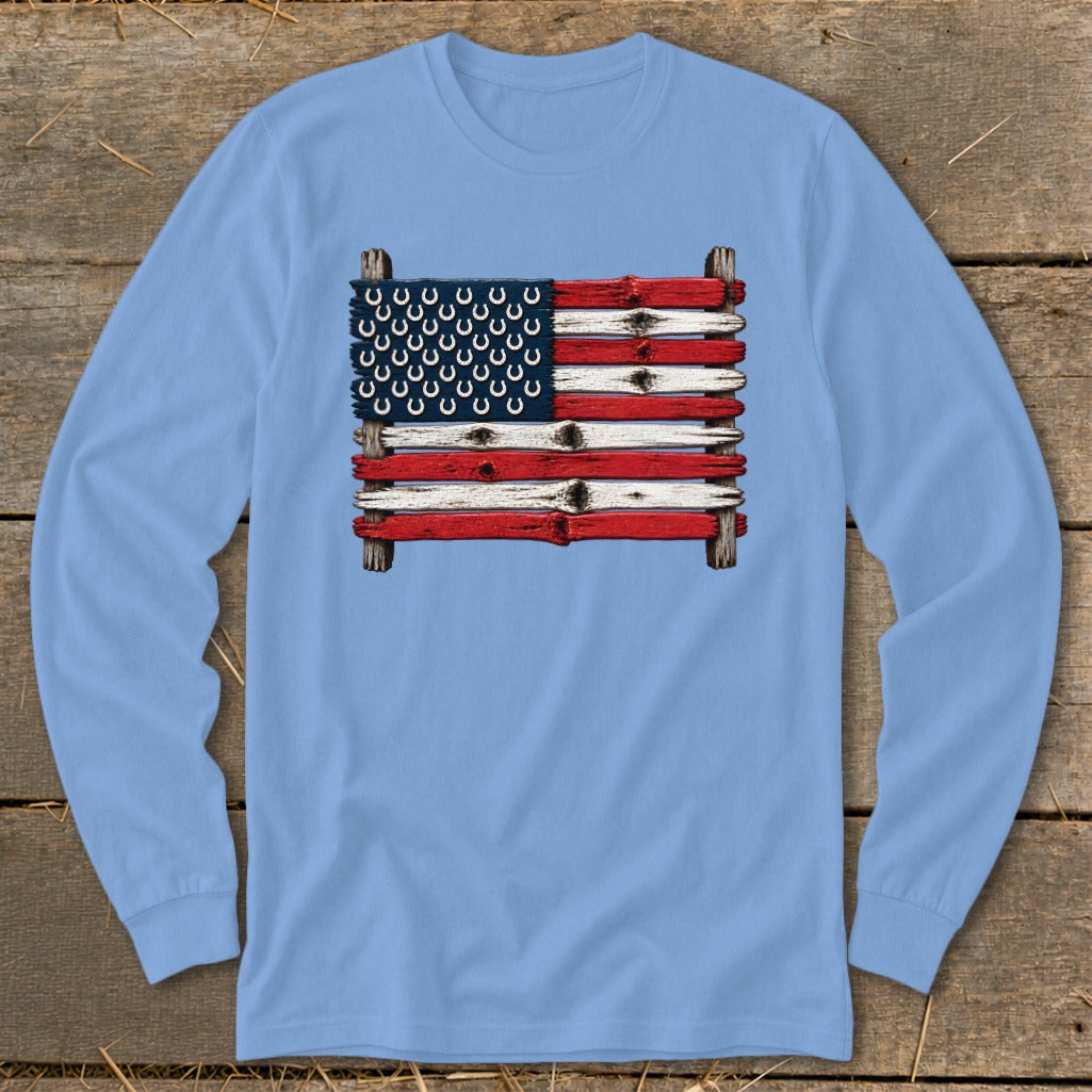 A light blue long-sleeve t-shirt featuring a graphic of the American flag made of rustic wooden planks and horseshoes.