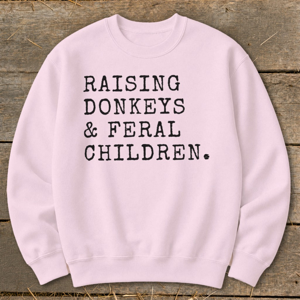 Pink crewneck sweatshirt with black text "RAISING DONKEYS & FERAL CHILDREN".