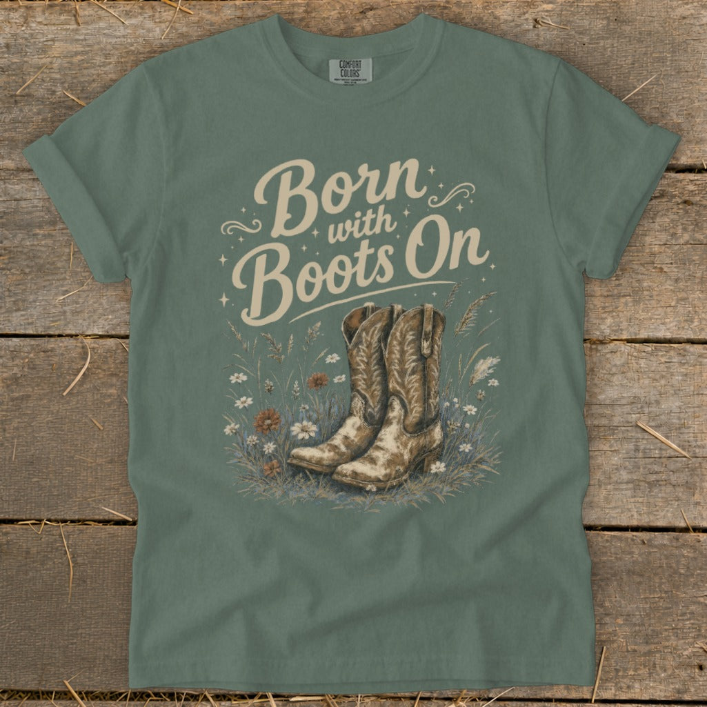 Green t-shirt with "Born with Boots On" text and cowboy boots in grass.