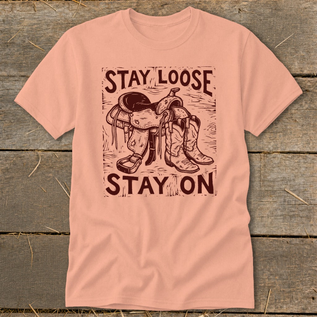 Peach t-shirt with "STAY LOOSE STAY ON" text and western saddle and boots graphic.