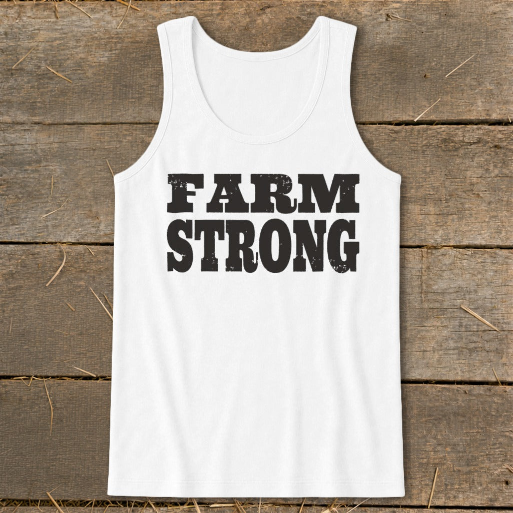 A white cotton tank top with the distressed black text "FARM STRONG" displayed on the chest, laid flat on a rustic wooden background.