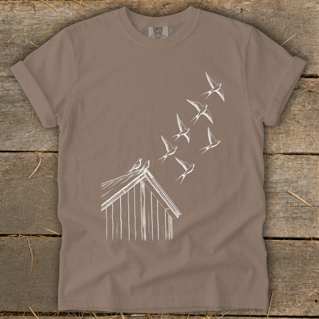 Brown crewneck t-shirt featuring a white line drawing of a barn and flock of swallows flying upward.