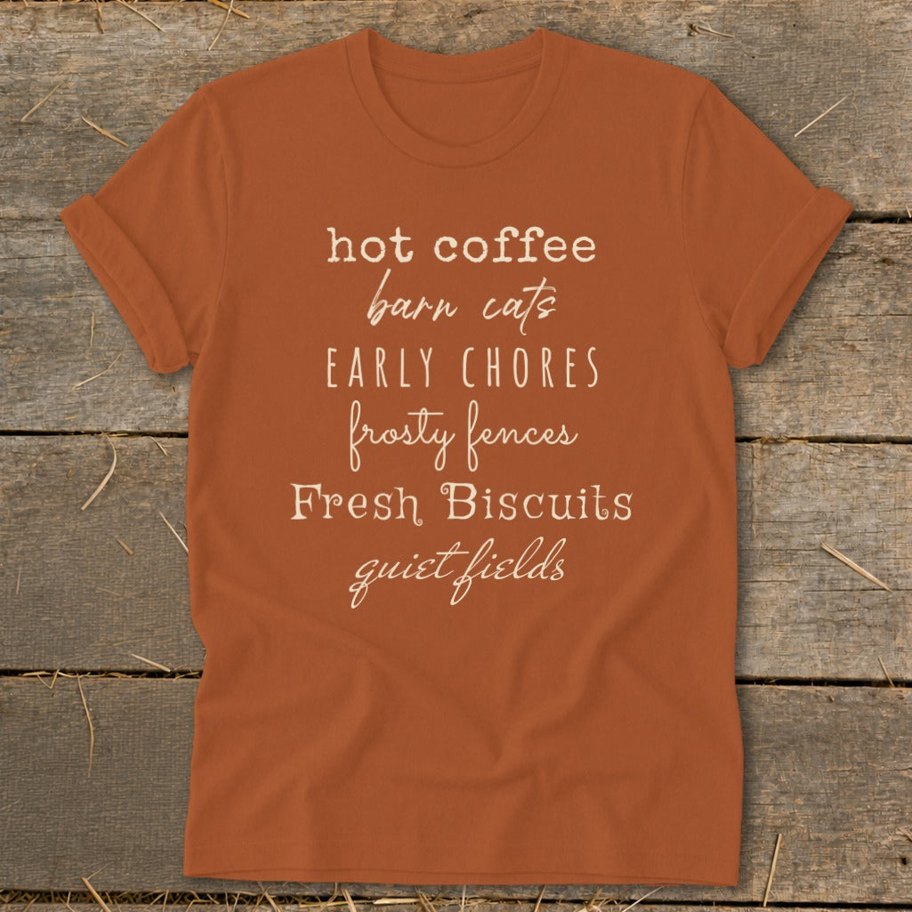 Orange t-shirt with white text listing: hot coffee, barn cats, early chores, frosty fences, fresh biscuits, quiet fields.