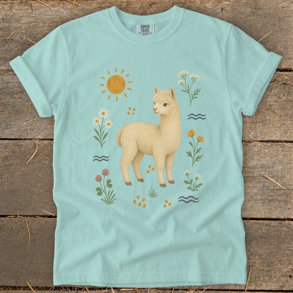 Light blue t-shirt with a cream alpaca, sun, flowers, and wavy lines design.