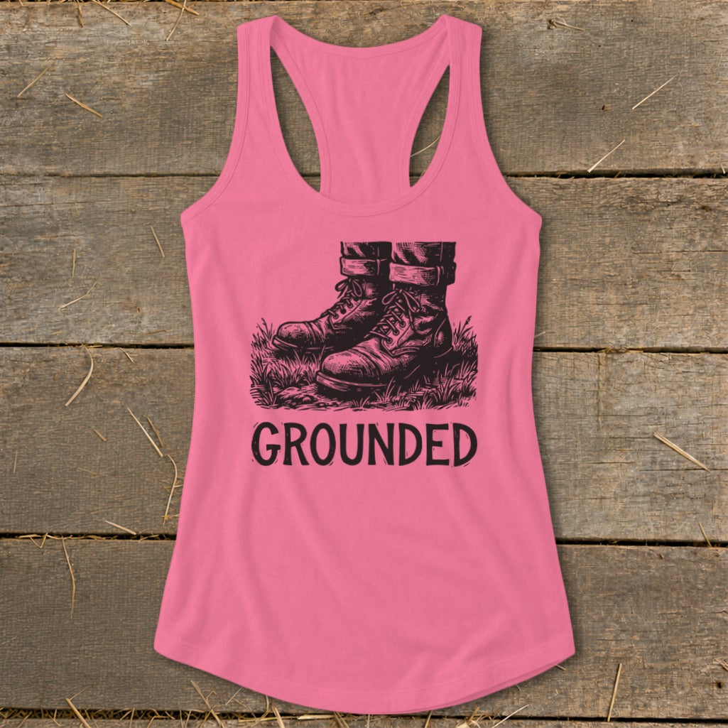Pink tank top with black graphic of boots in grass and text "GROUNDED".