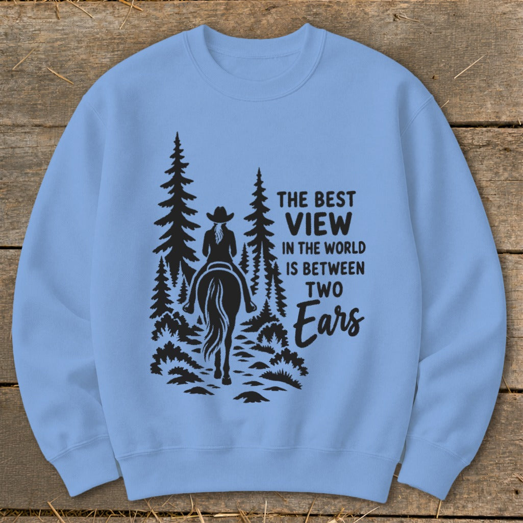 Light blue crewneck sweatshirt featuring a black graphic of a horseback rider amid pine trees and text reading The Best View in the World Is Between Two Ears.
