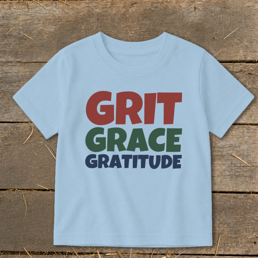 Light blue t-shirt featuring the text GRIT GRACE GRATITUDE in red, green, and blue.