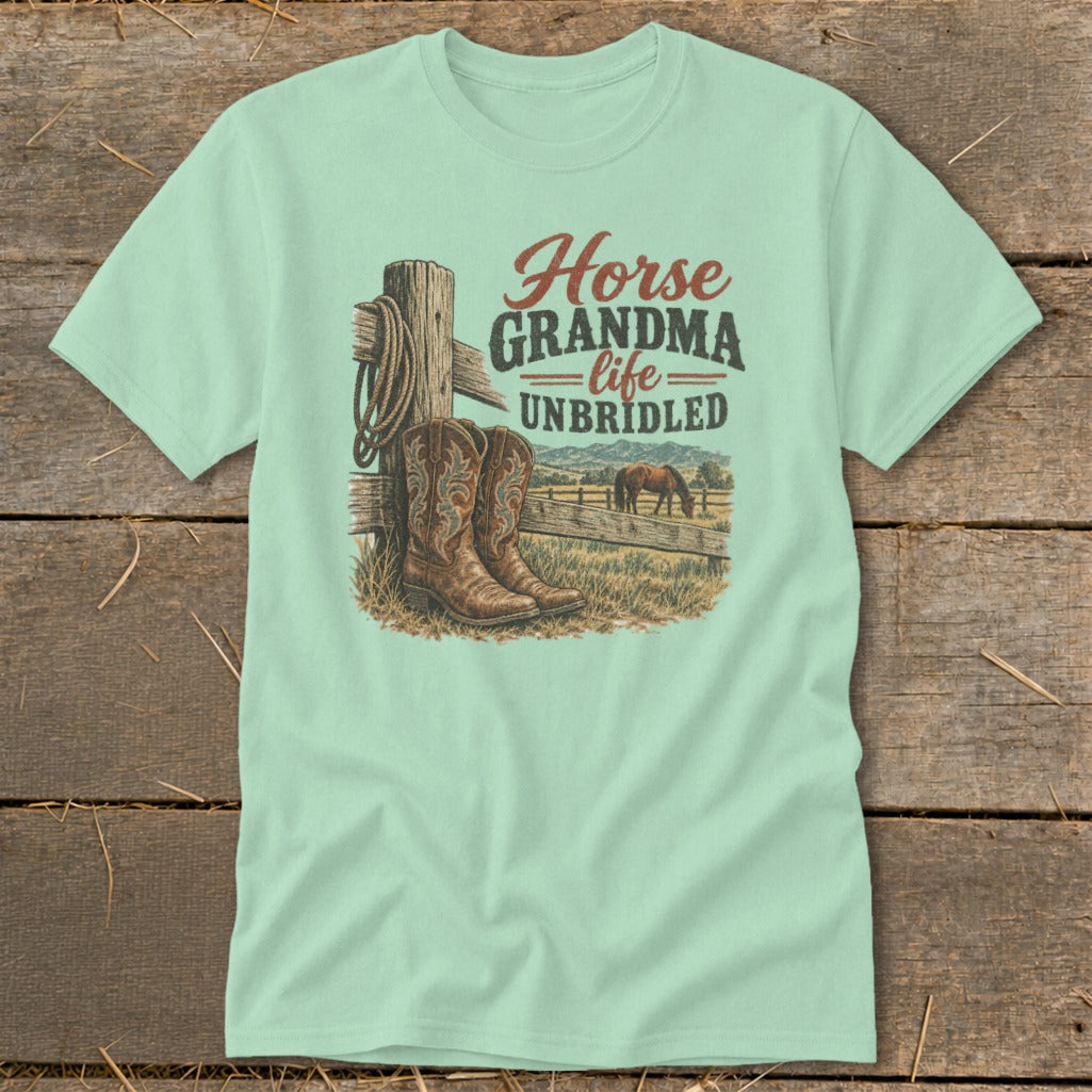 A light green t-shirt with a graphic showing cowboy boots, a fence, and the text Horse Grandma Life Unbridled.