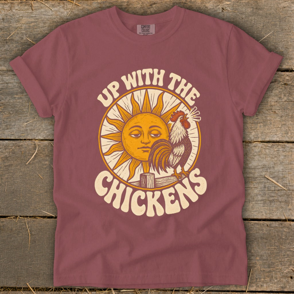 Dusty rose short-sleeve t-shirt with a vintage-style graphic of a rooster, a sun, and the text Up With The Chickens.