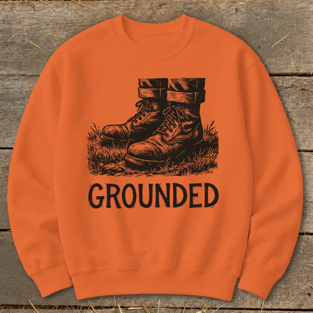 Orange sweatshirt with black graphic of boots in grass and the word "GROUNDED".