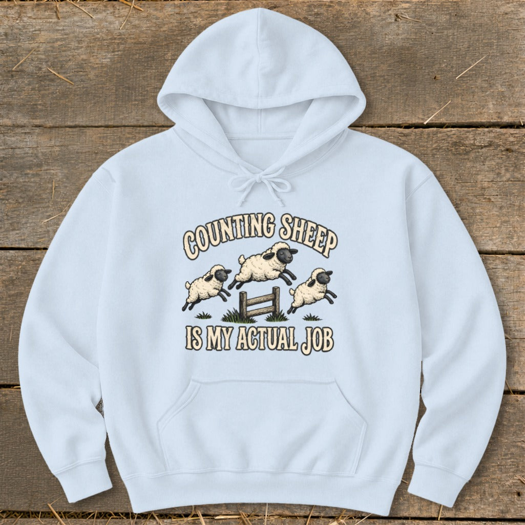 Light blue hoodie with a graphic of sheep jumping over a fence and text that reads "COUNTING SHEEP IS MY ACTUAL JOB".