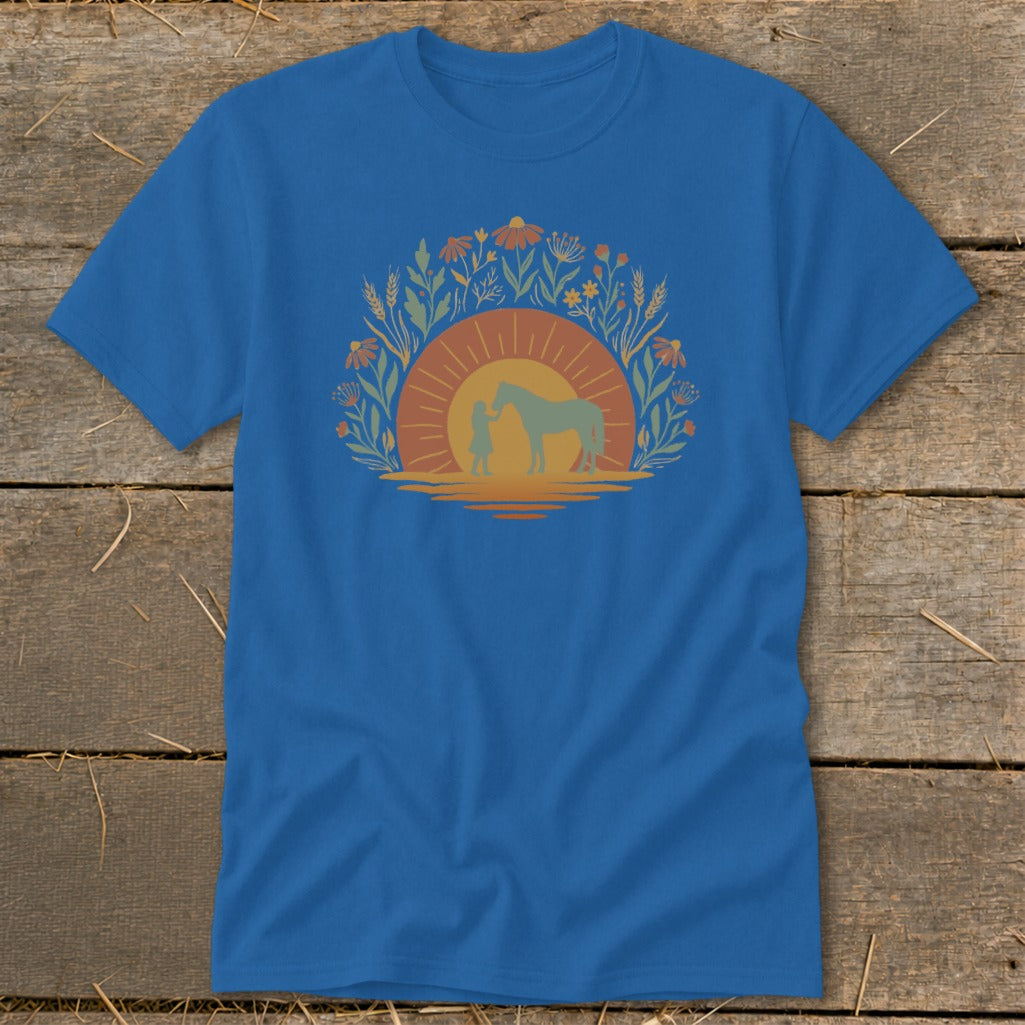 Blue t-shirt with a graphic of a person and horse at sunset surrounded by flowers.