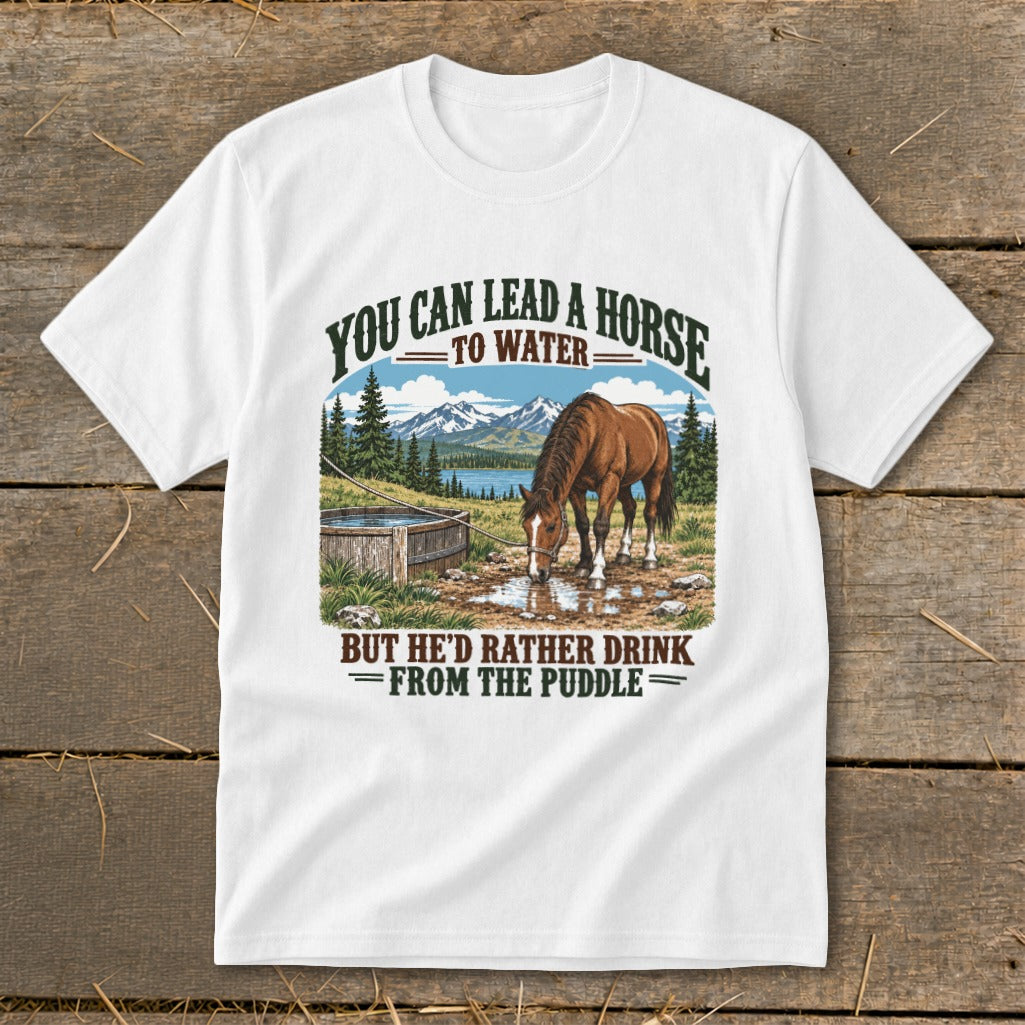 A white t-shirt featuring graphic text and an illustration of a brown horse drinking from a puddle near a wooden trough, with mountains and trees in the background.