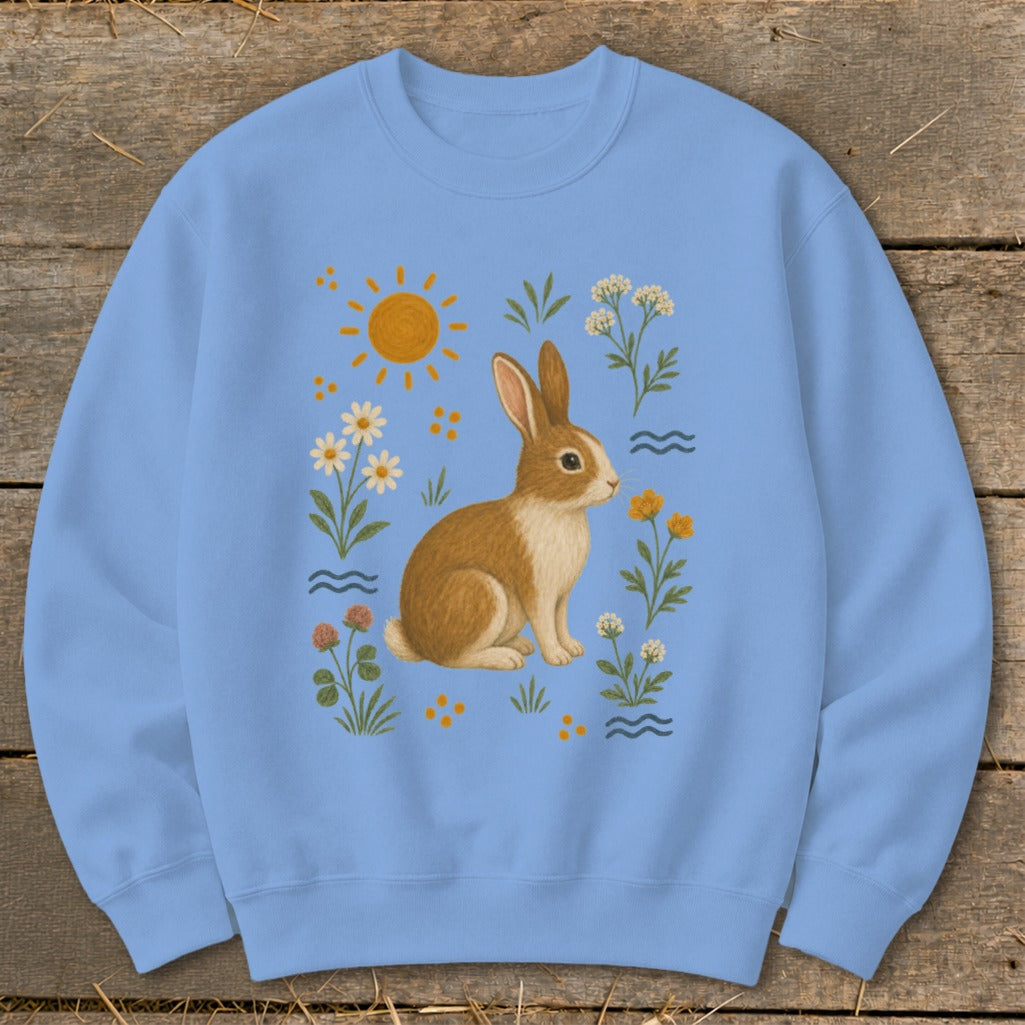 Light blue sweatshirt with a brown and white rabbit surrounded by flowers and the sun.