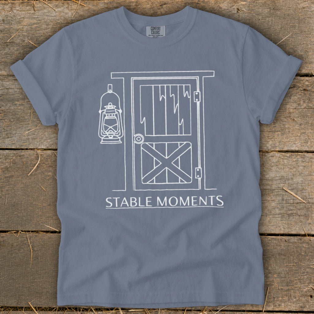Blue t-shirt with white line drawing of barn door and lantern, text "STABLE MOMENTS".
