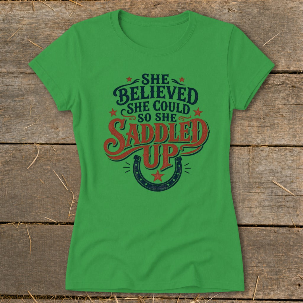 Green t-shirt with "She believed she could so she saddled up" text and horseshoe design.