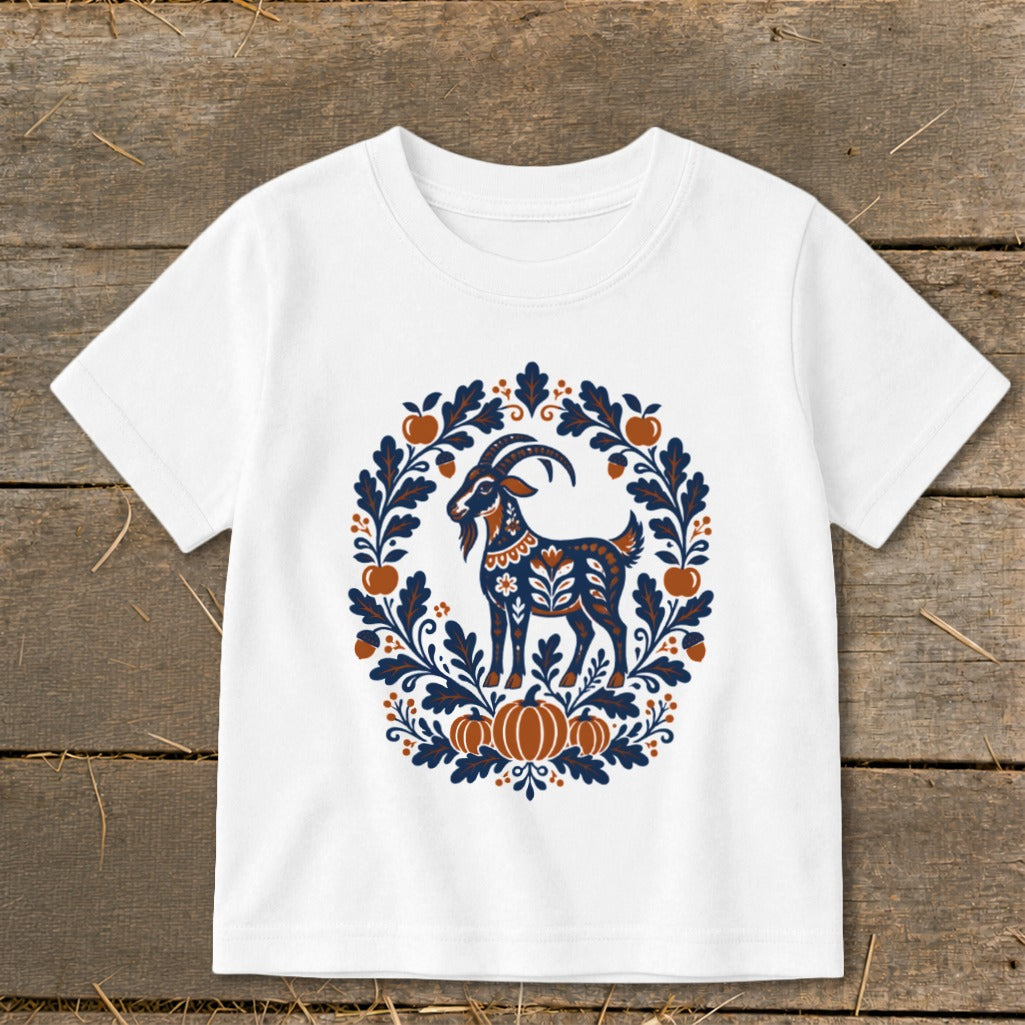 A white short-sleeved t-shirt features a folk-art graphic of a goat surrounded by autumn leaves and pumpkins.