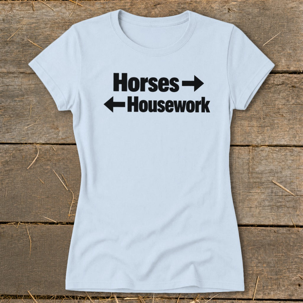 A light blue women's t-shirt printed with black text that reads Horses pointing right and Housework pointing left.