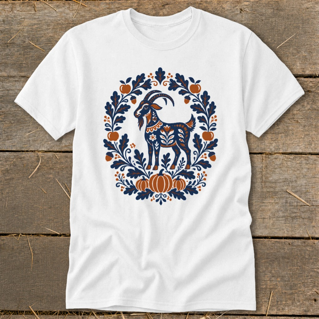 A white t-shirt featuring a blue and rust folk-art goat graphic surrounded by leaves, acorns, and pumpkins.
