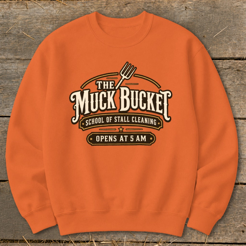 Orange sweatshirt with "The Muck Bucket School of Stall Cleaning Opens at 5 AM" logo.