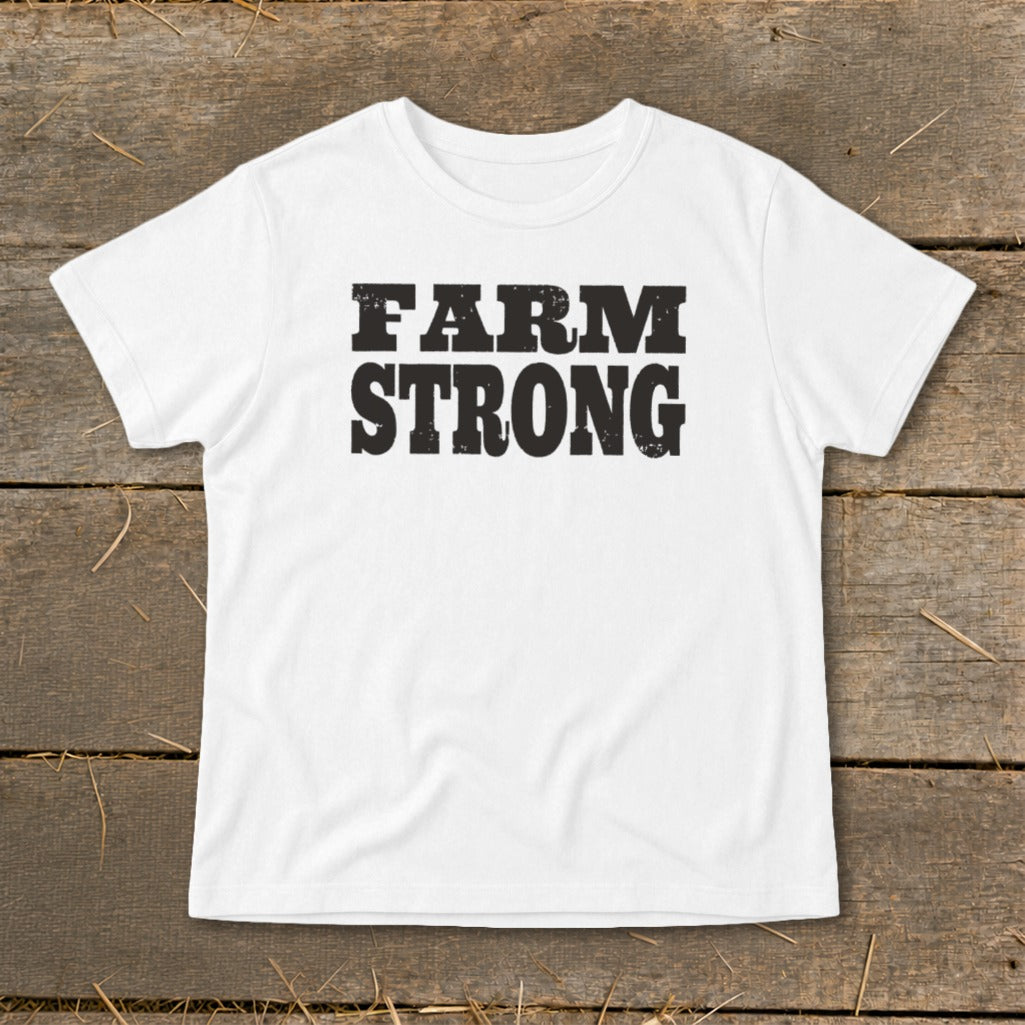 White short-sleeved t-shirt with bold black text reading FARM STRONG centered on the chest, laid flat on wooden boards.