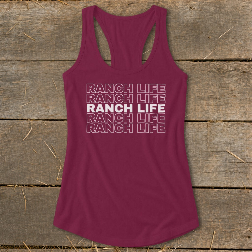Maroon racerback tank top with repeated white block text reading "RANCH LIFE" laid on a rustic wooden background.