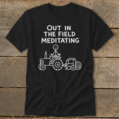 Black t-shirt with white text "OUT IN THE FIELD MEDITATING" and a drawing of a stick figure meditating on a tractor.