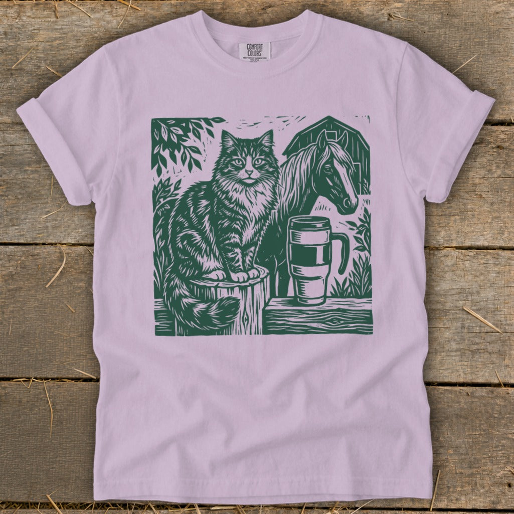 Cat, horse, and mug graphic print on a light purple t-shirt.