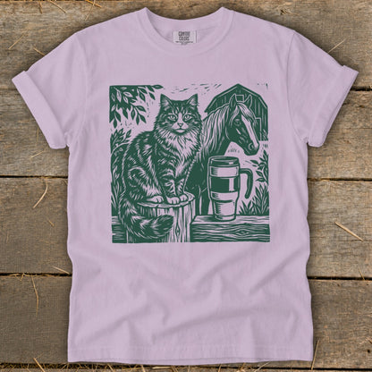 Cat, horse, and mug graphic print on a light purple t-shirt.