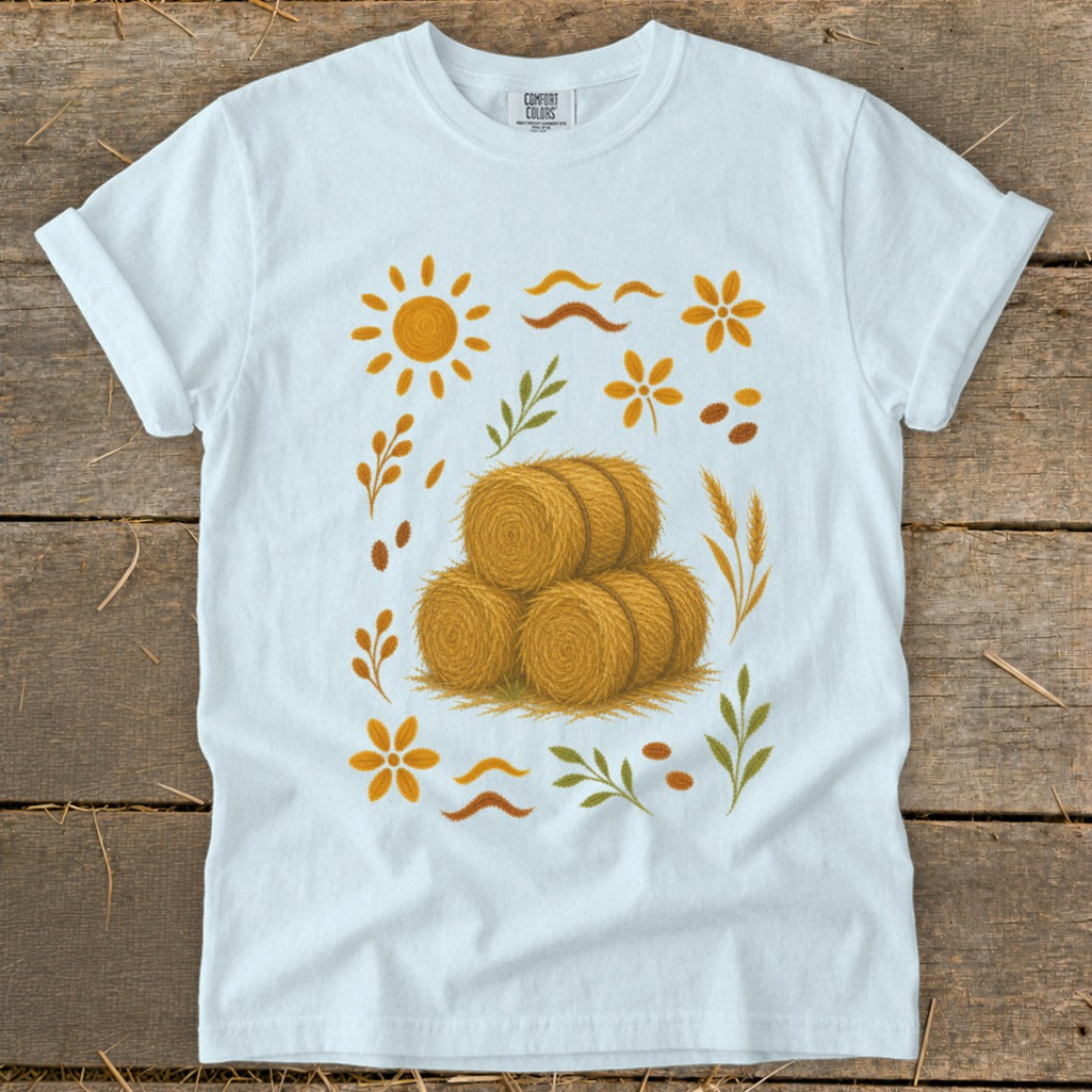 White t-shirt with a graphic featuring hay bales surrounded by autumn-themed elements.