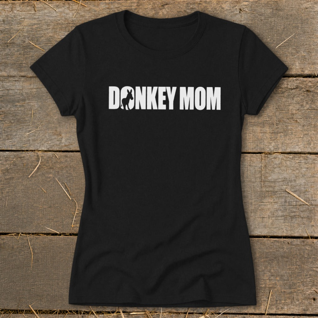 A black women's crew neck t-shirt featuring the white text DONKEY MOM with a donkey silhouette inside the letter O, laid on wooden boards.