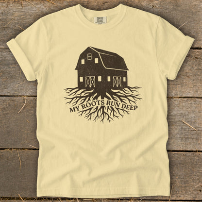 Pale yellow t-shirt with dark brown barn and roots graphic, text "MY ROOTS RUN DEEP."